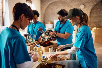 Groupe multiracial de bénévoles emballant des produits d'épicerie dans une banque alimentaire communautaire.